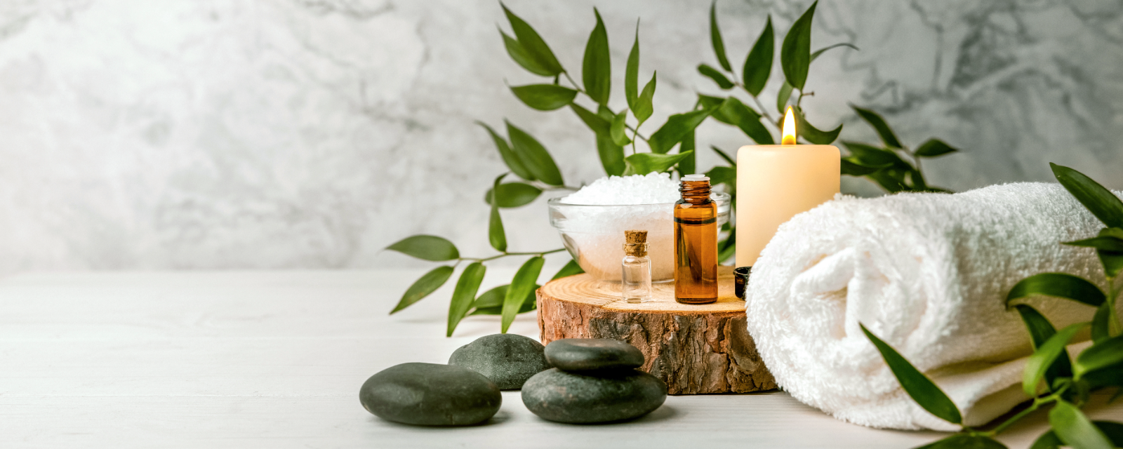 Spa wellness arrangement with candle, essential oils, stones, towels and greenery