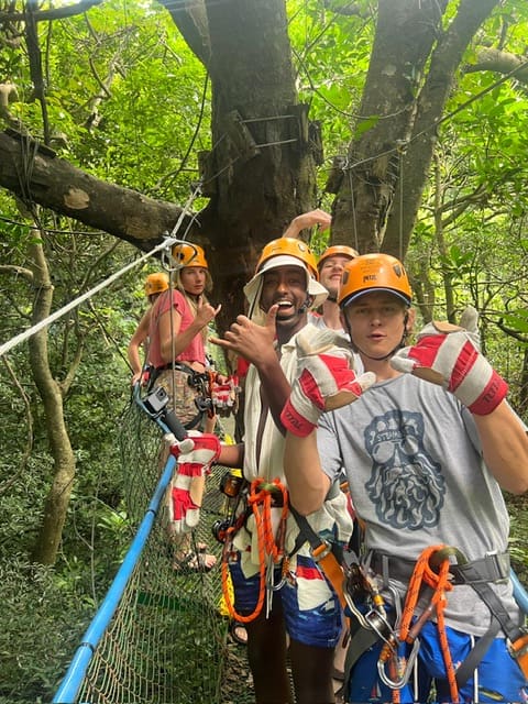 Group of people wearing safety helmets and harnesses on a canopy tour through dense green forest