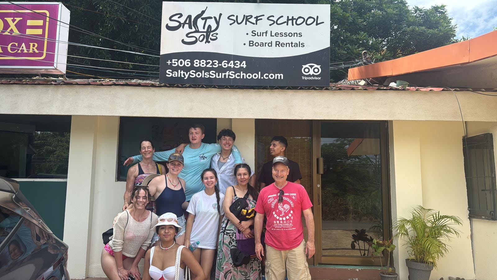 Group of surfers posing outside Salty Sols Surf School storefront with signage