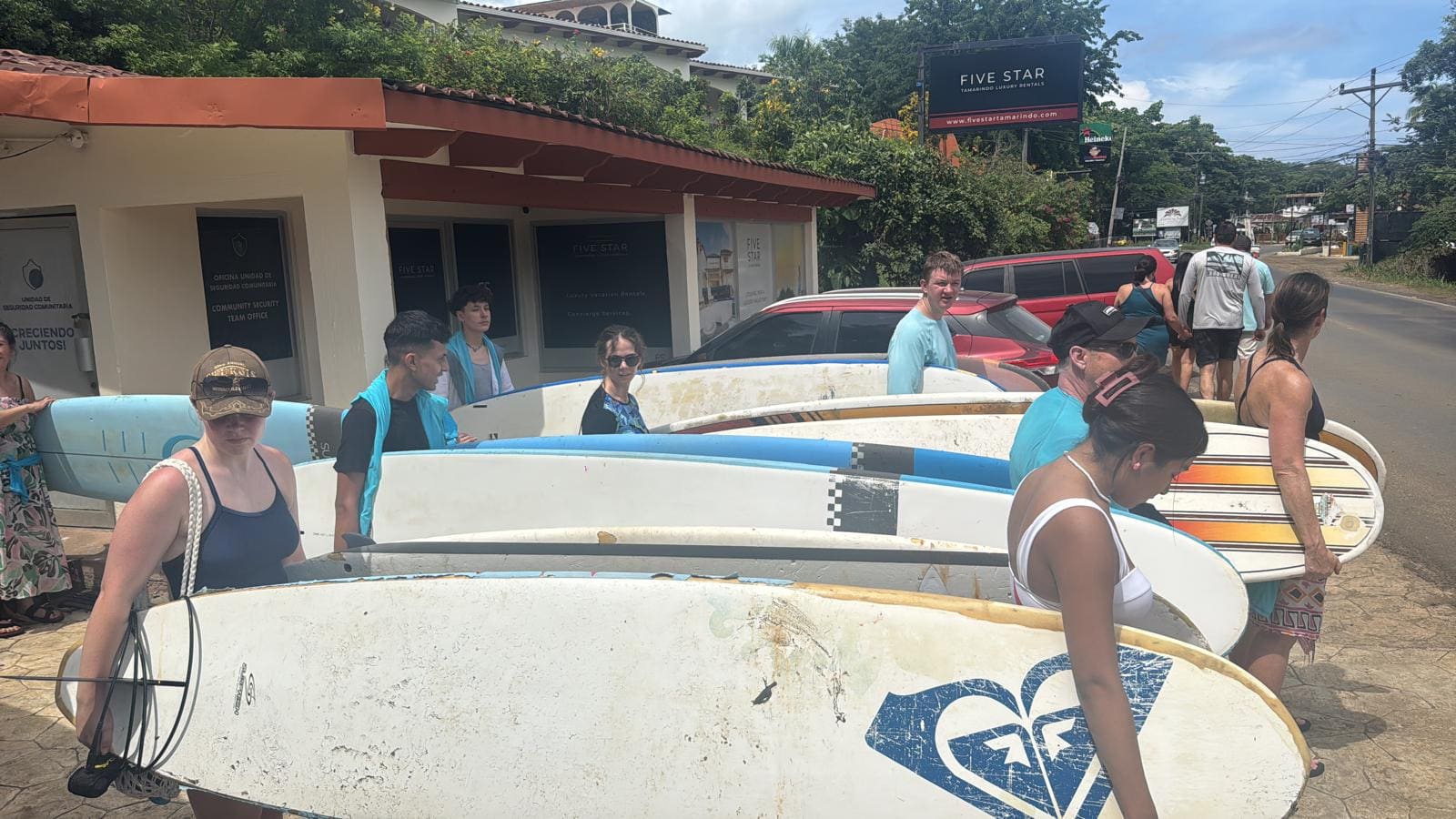Group of tourists holding surfboards outside Five Star shop in tropical location
