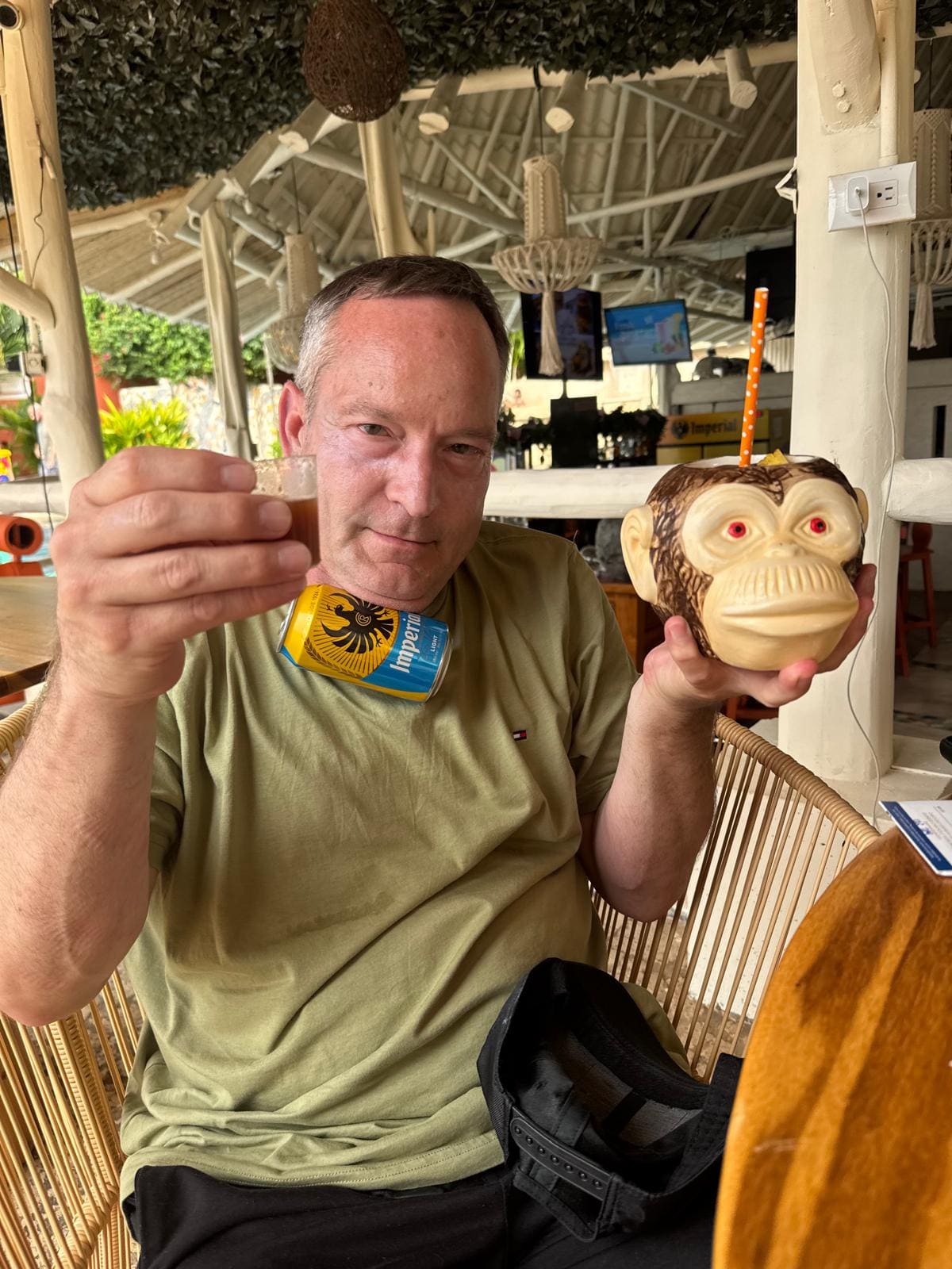 Man holding a monkey figurine and beer bottle in a beachside venue