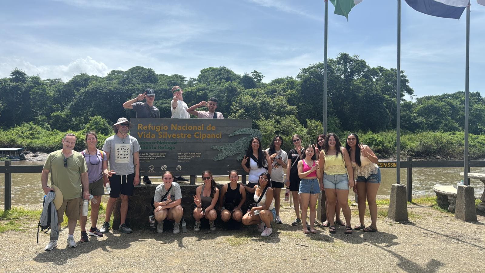 Group of tourists posing at Cipanci National Wildlife Refuge sign by river in tropical setting