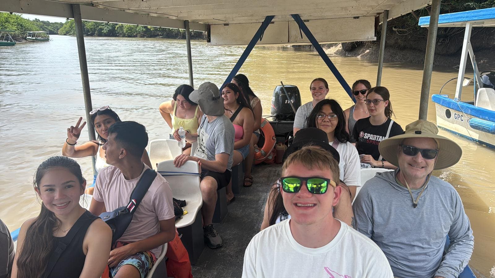 Group of tourists on a covered boat tour in murky river water surrounded by mangroves