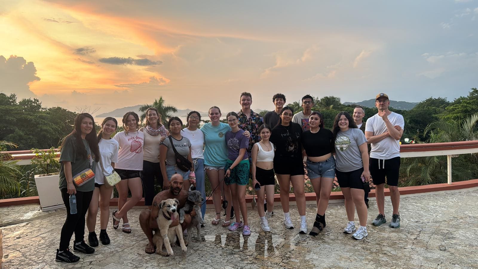 Group of people and a dog posing on a terrace at sunset with mountains and tropical vegetation in background