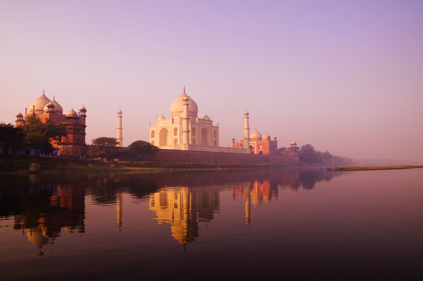Taj Mahal reflected in the Yamuna River at sunrise with pink sky and morning mist