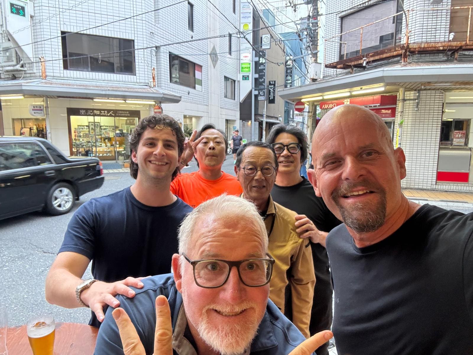 Group of six people smiling at camera on a Japanese street with storefronts and buildings behind them