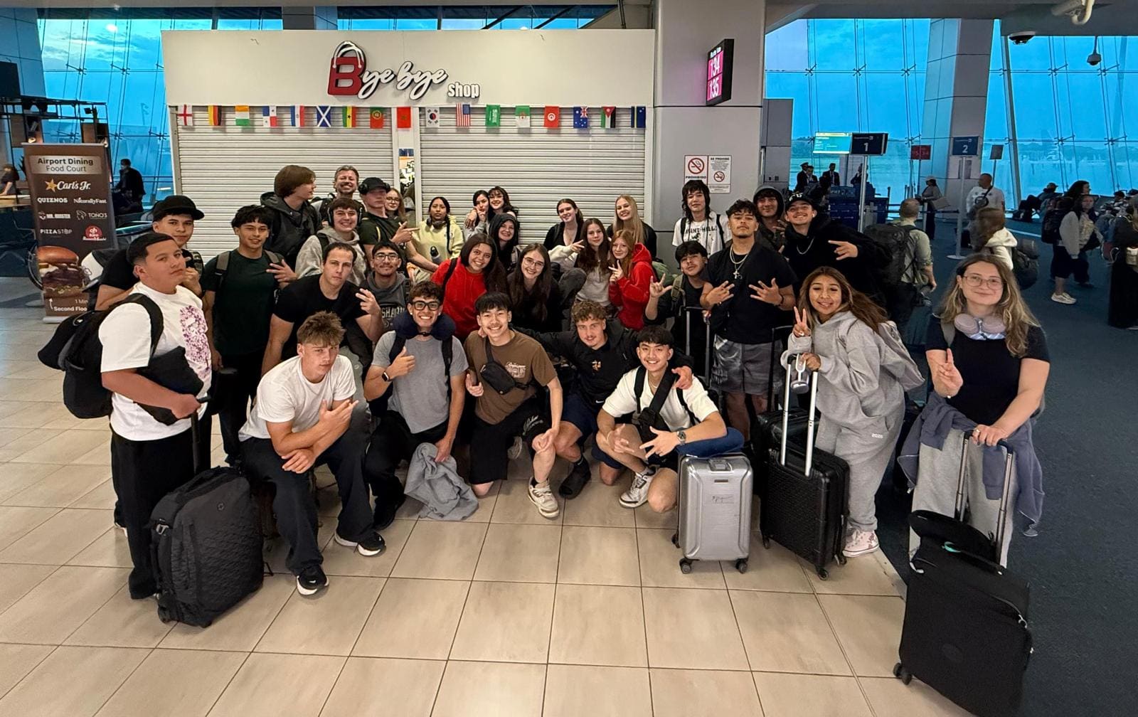 Large group of young travelers posing together at an airport terminal with luggage