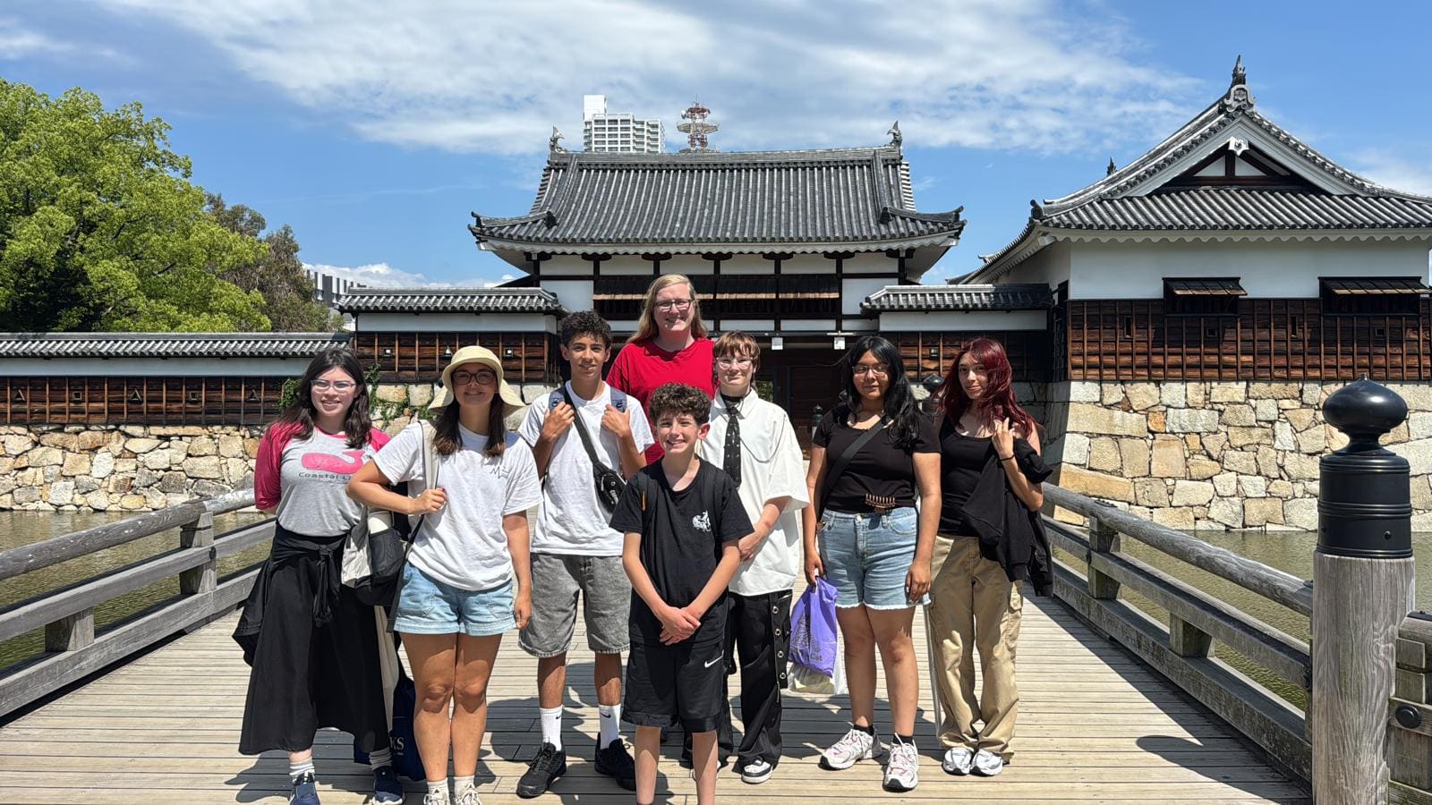 Group of eight people standing on wooden bridge in front of traditional Japanese temple buildings