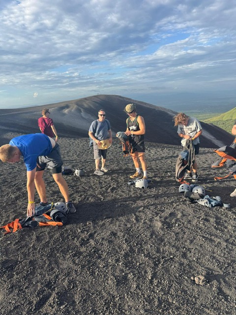 Group of hikers gathered on volcanic crater rim with dark cone mountain in background