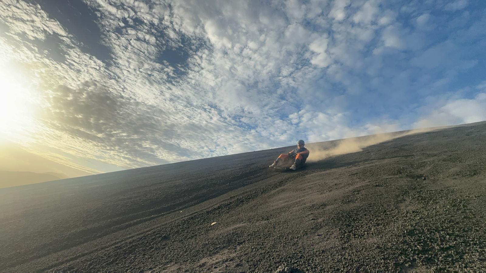Person sitting on volcanic black sand slope under cloudy sky