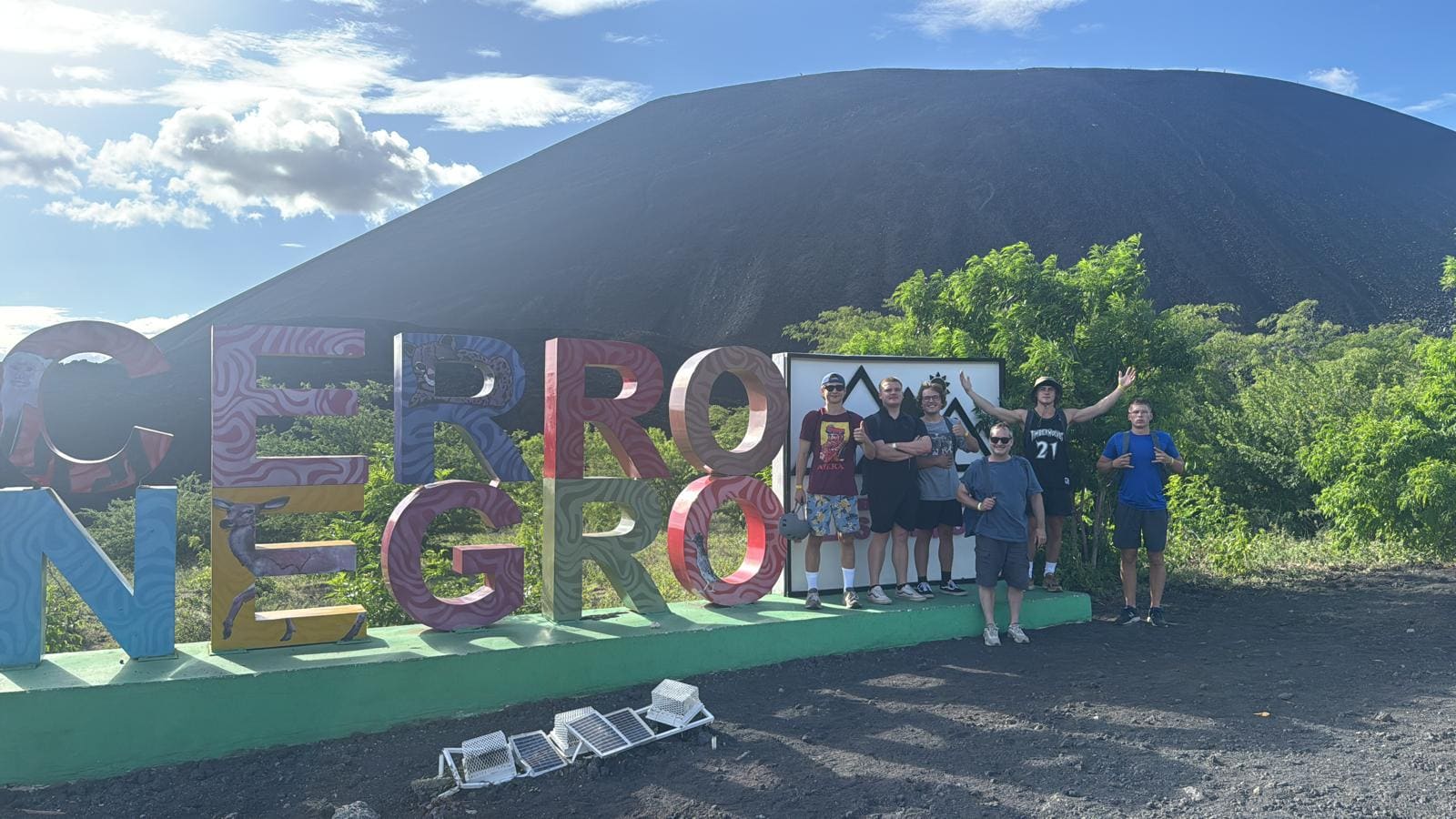 Group of visitors posing at colorful Cerro Negro sign with volcanic mountain backdrop