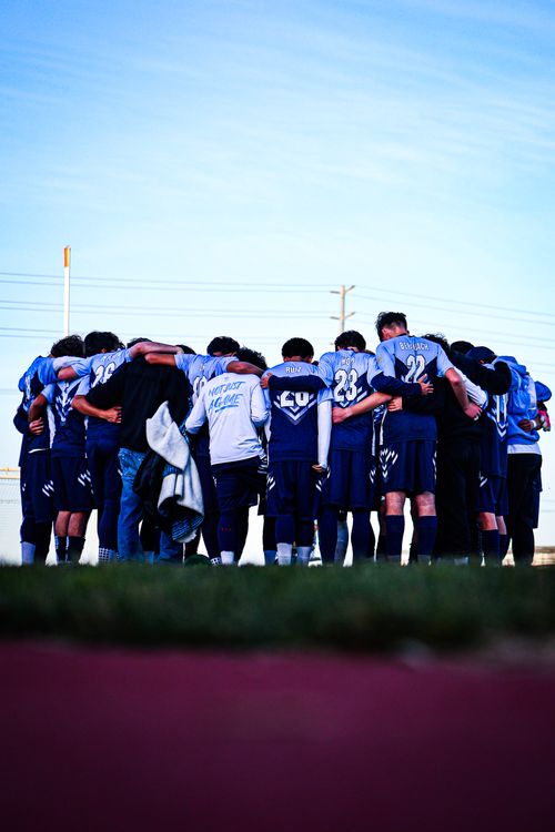 Youth soccer team in blue jerseys huddled together on field before game